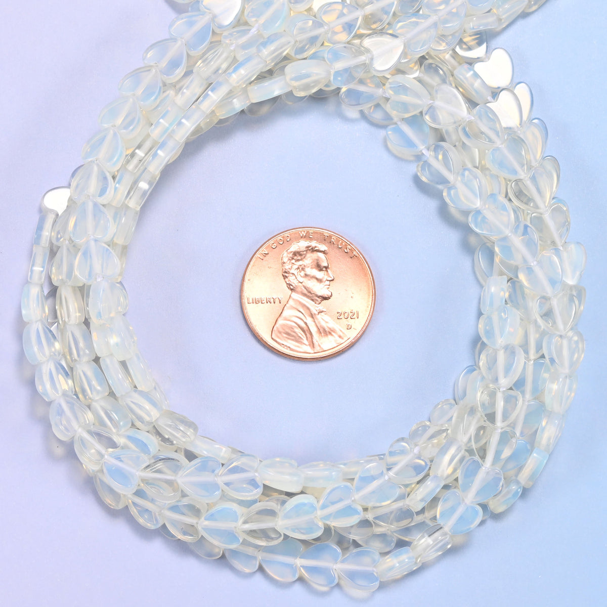 Opalite flat heart bead strands coiled around a US penny for size reference