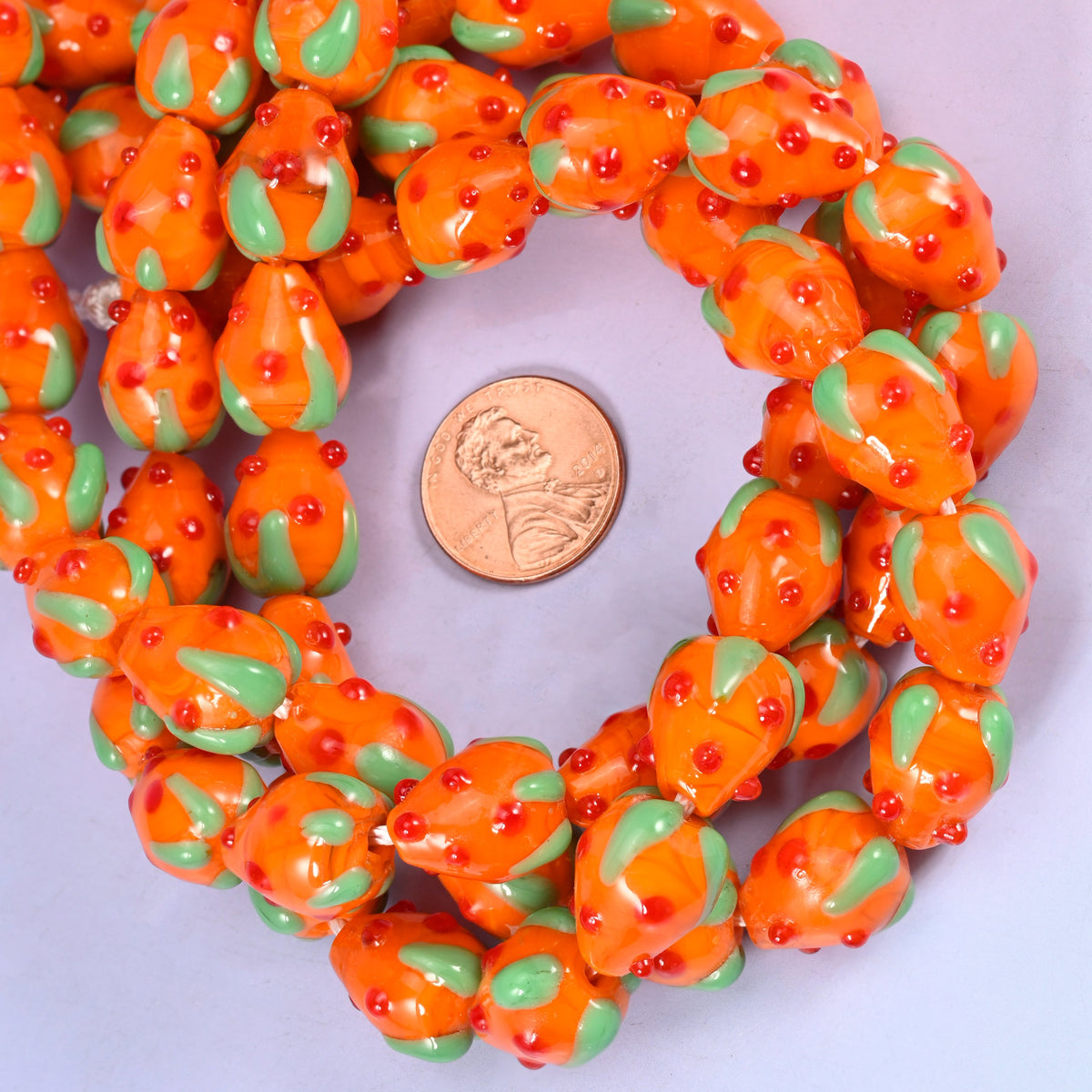 Orange Red Dots Strawberry glass bead strands coiled around a US penny for size reference
