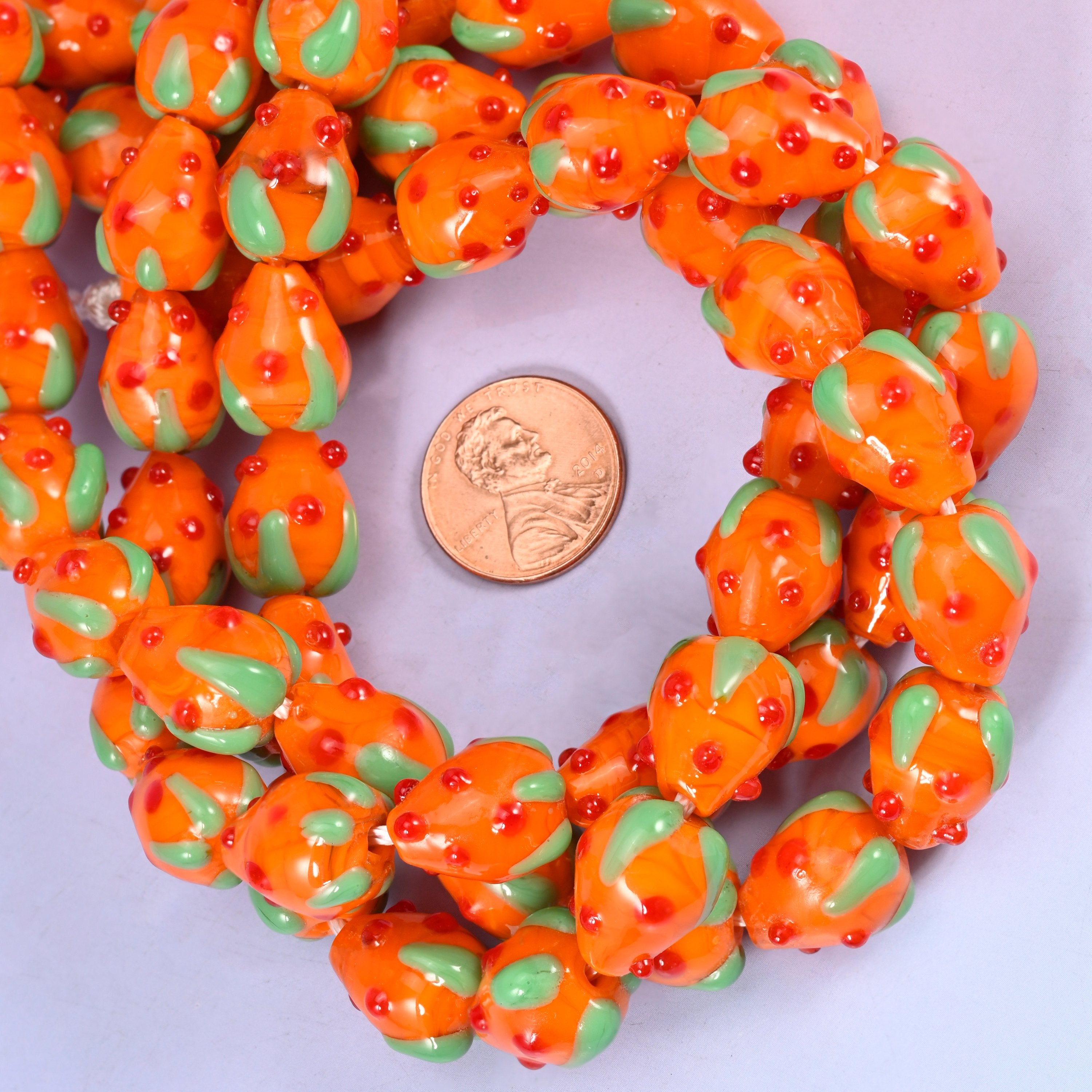 Orange Red Dots Strawberry glass bead strands coiled around a US penny for size reference