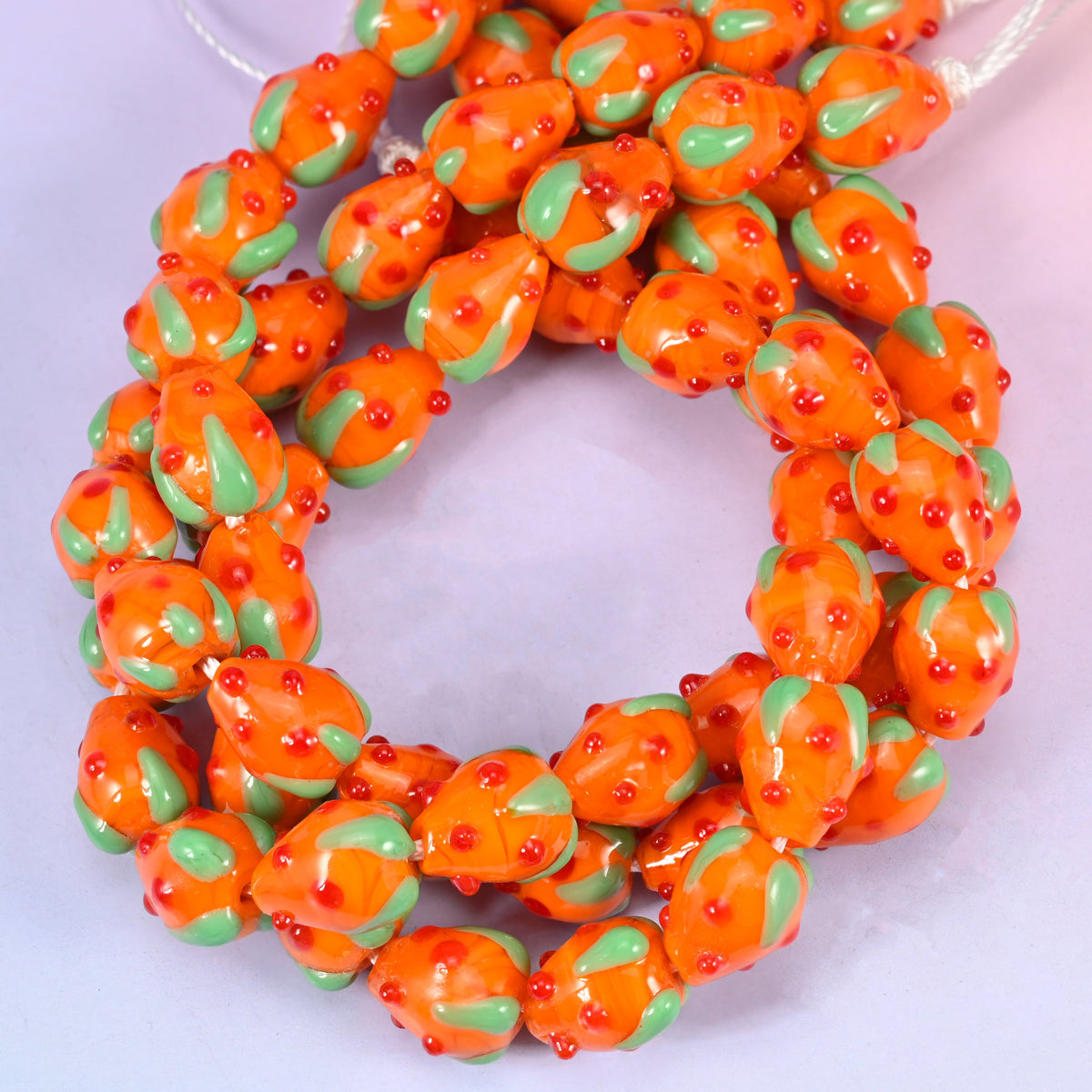 Orange Red Dots Strawberry glass beads, close view of the coiled strands in orange with green leaf panels and raised red seed dots