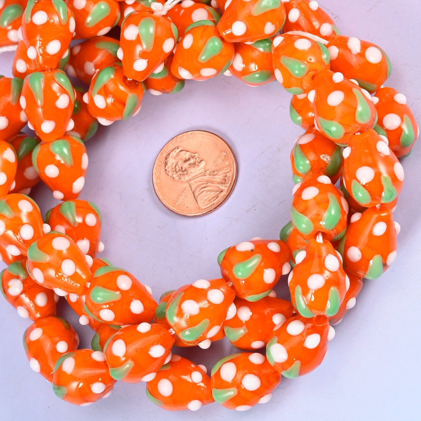 Orange White Dots Strawberry glass bead strands coiled around a US penny for size reference