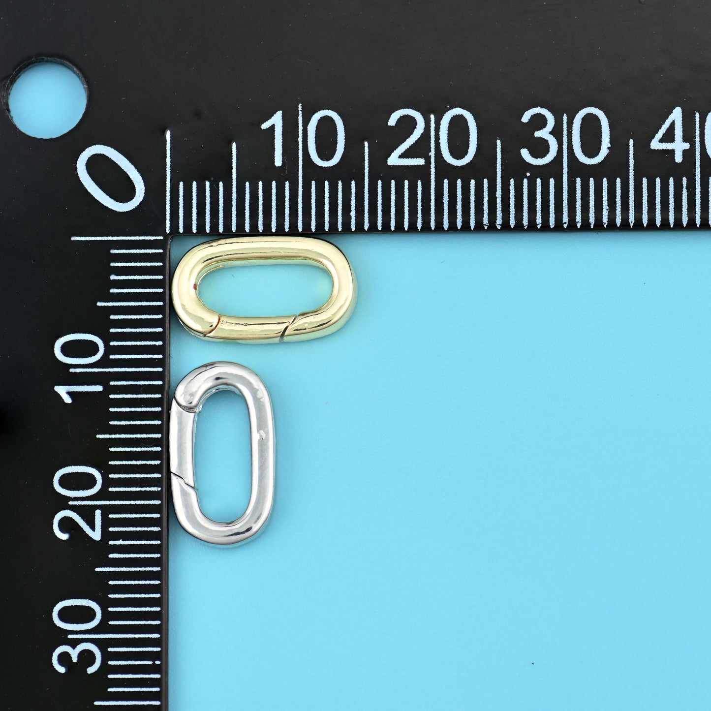Gold and silver oval carabiner clasps beside a millimetre ruler for scale