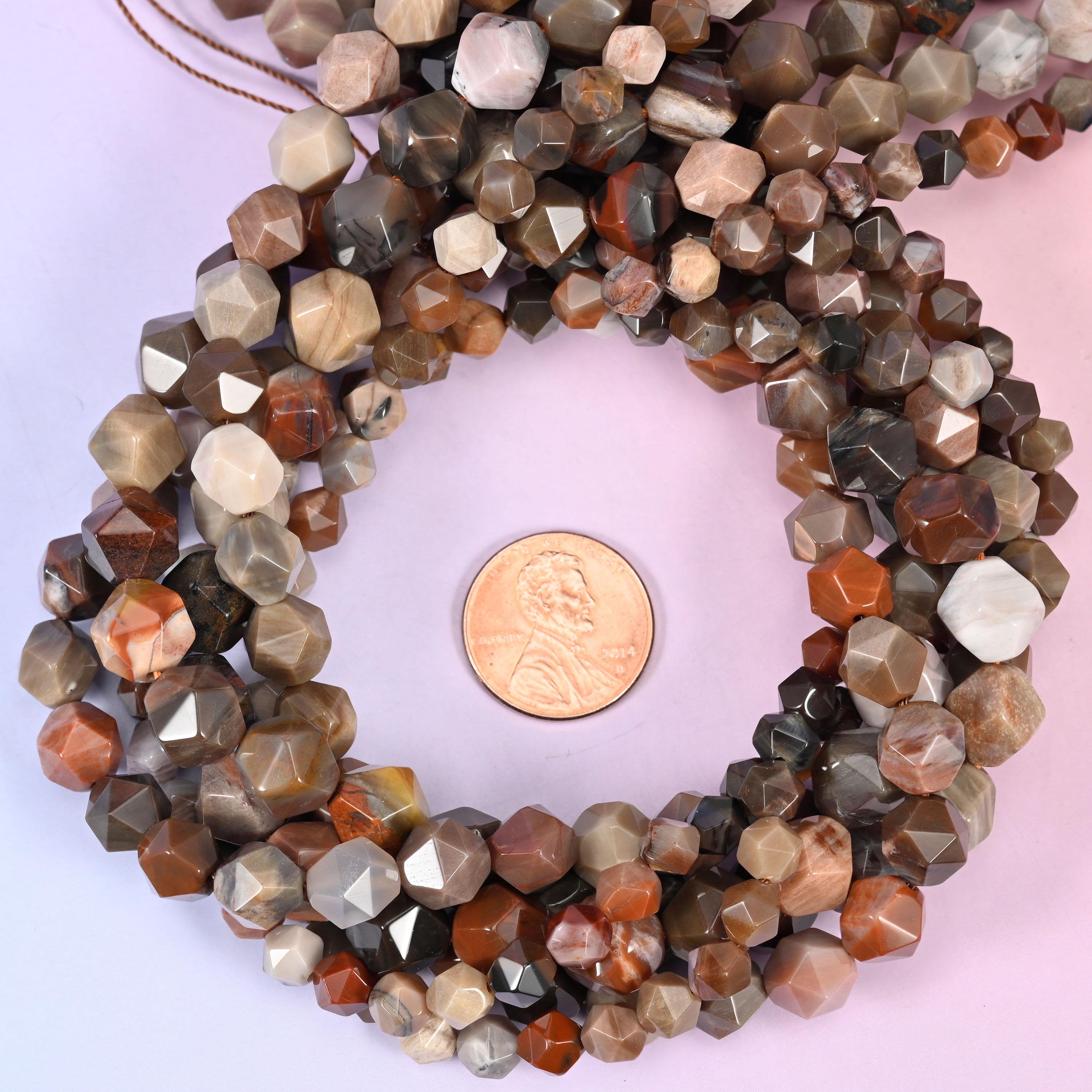 Petrified Wood faceted diamond star cut bead strands coiled around a US penny for size reference