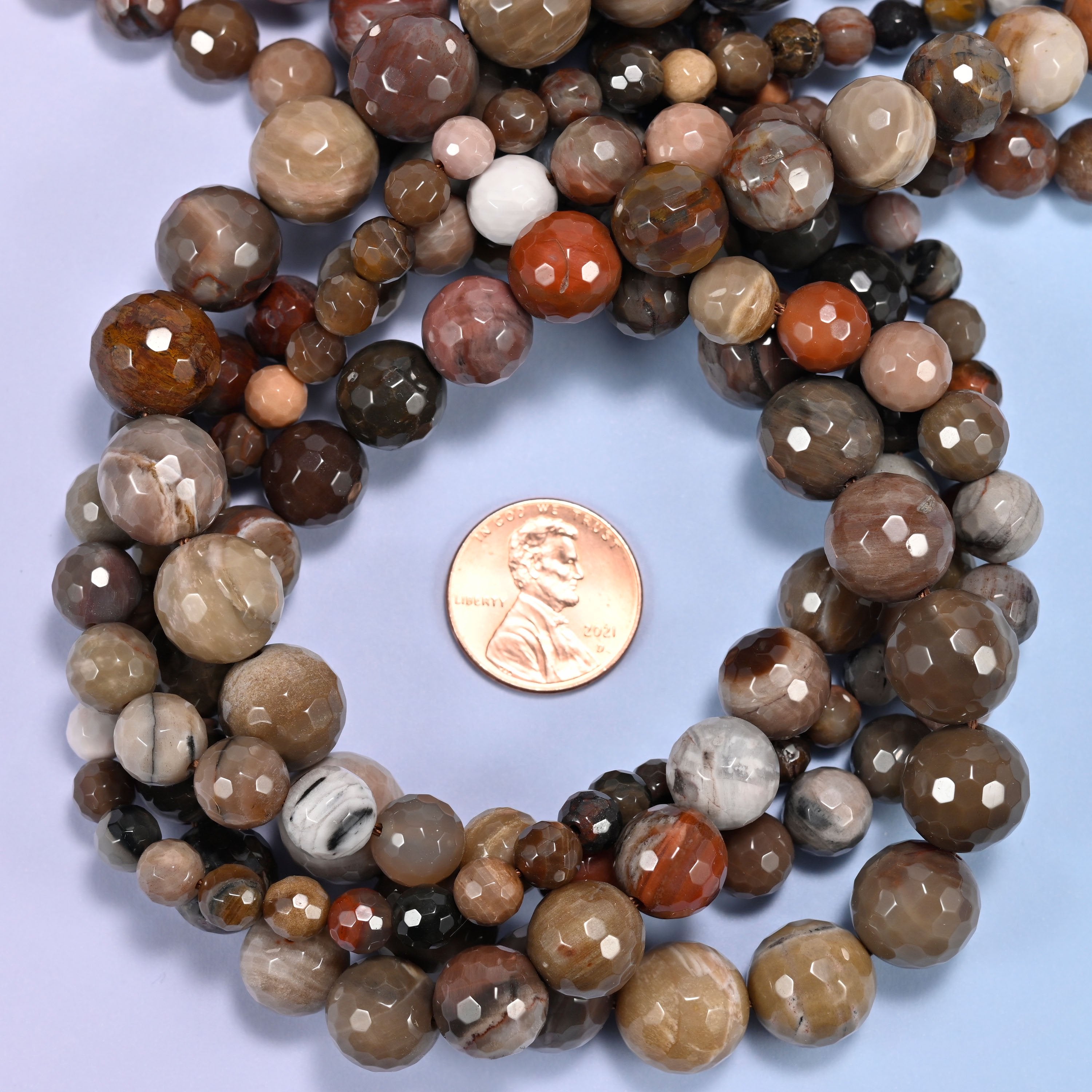 Petrified Wood faceted round bead strands coiled around a US penny for size reference