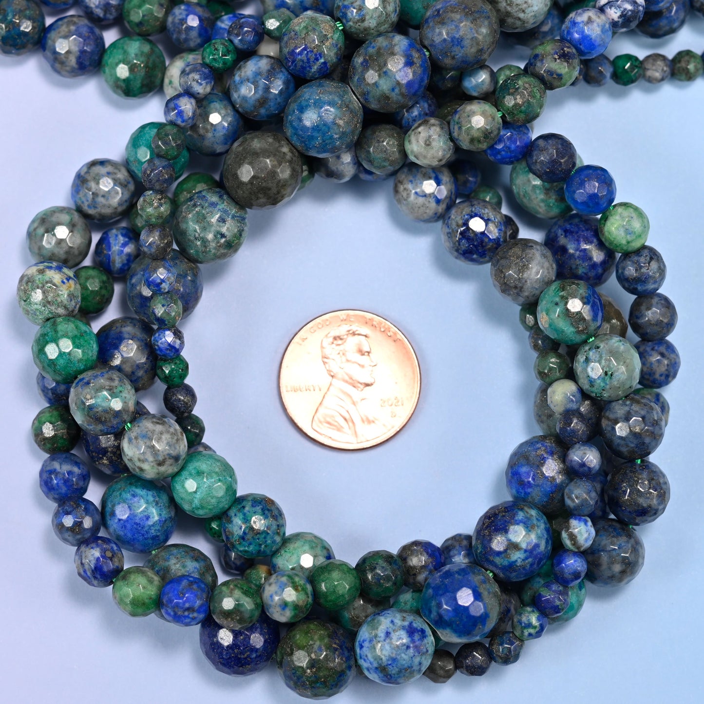 Phoenix Lapis faceted round bead strands coiled around a US penny for size reference