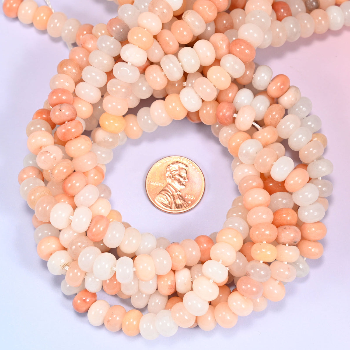 Pink Aventurine rondelle bead strands coiled around a US penny for size reference