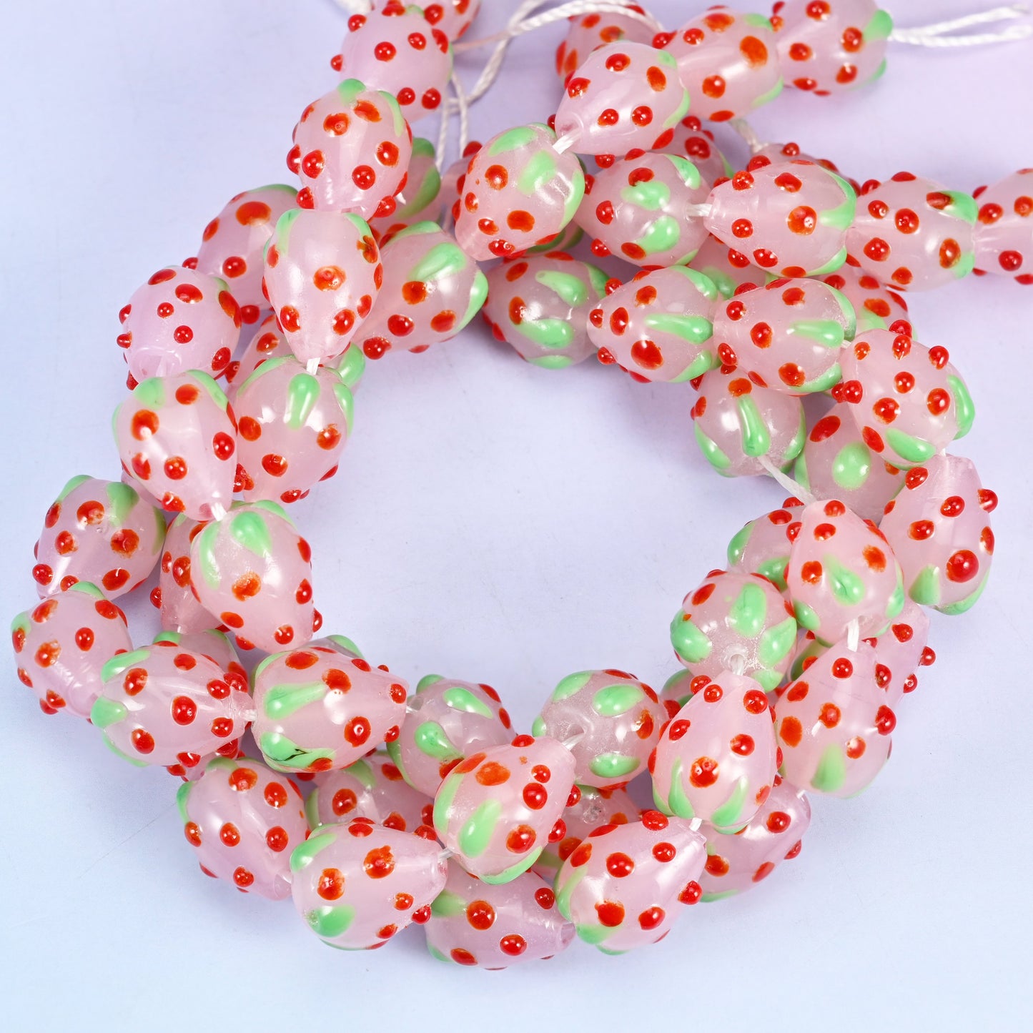 Pink Red Dots Strawberry glass beads, close view of the coiled strands in soft pink with green leaf panels and red seed dots