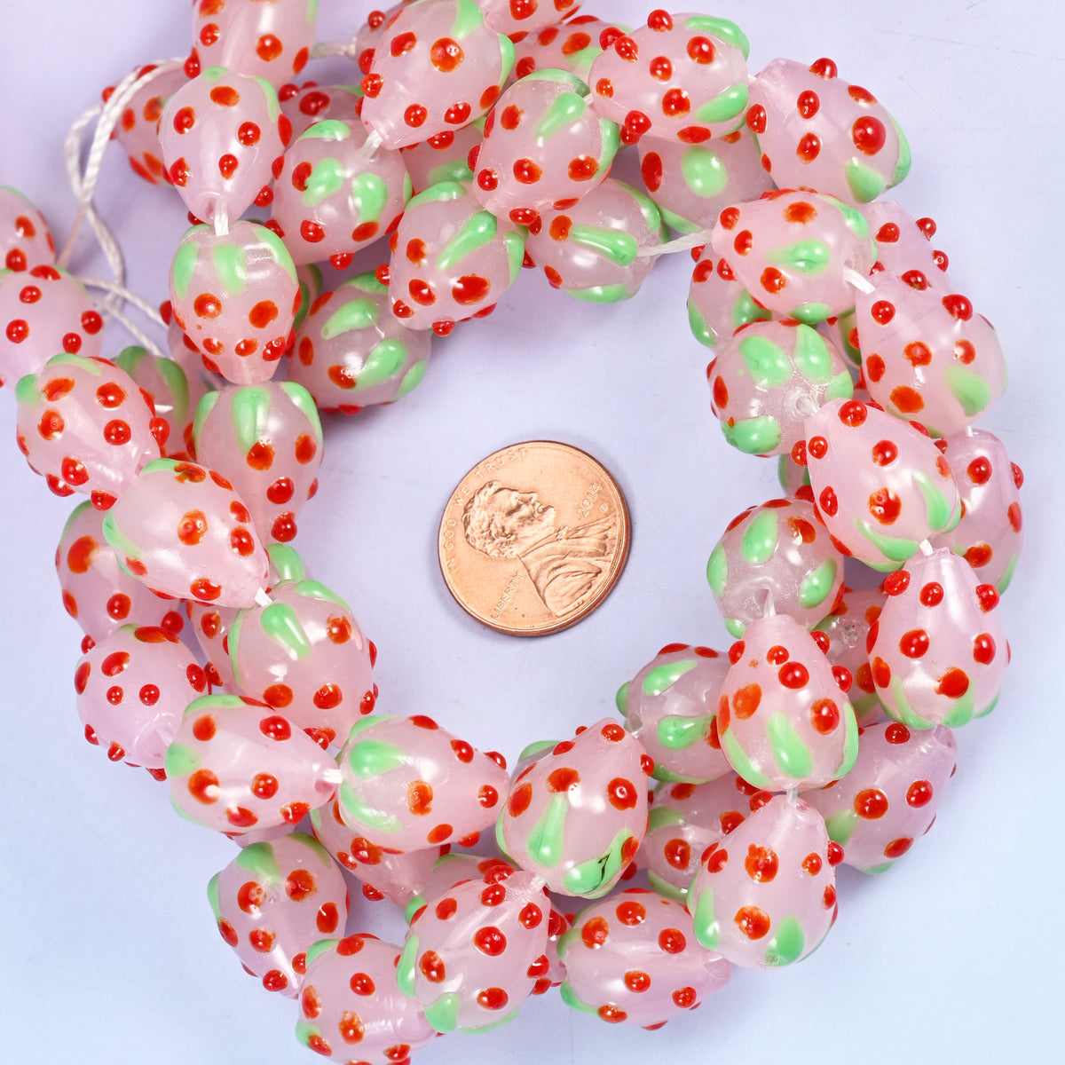 Pink Red Dots Strawberry glass bead strands coiled around a US penny for size reference