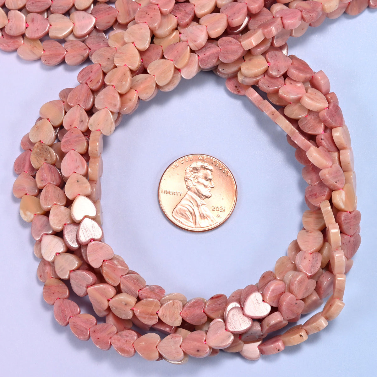 Pink Rhodonite flat heart bead strands coiled around a US penny for size reference