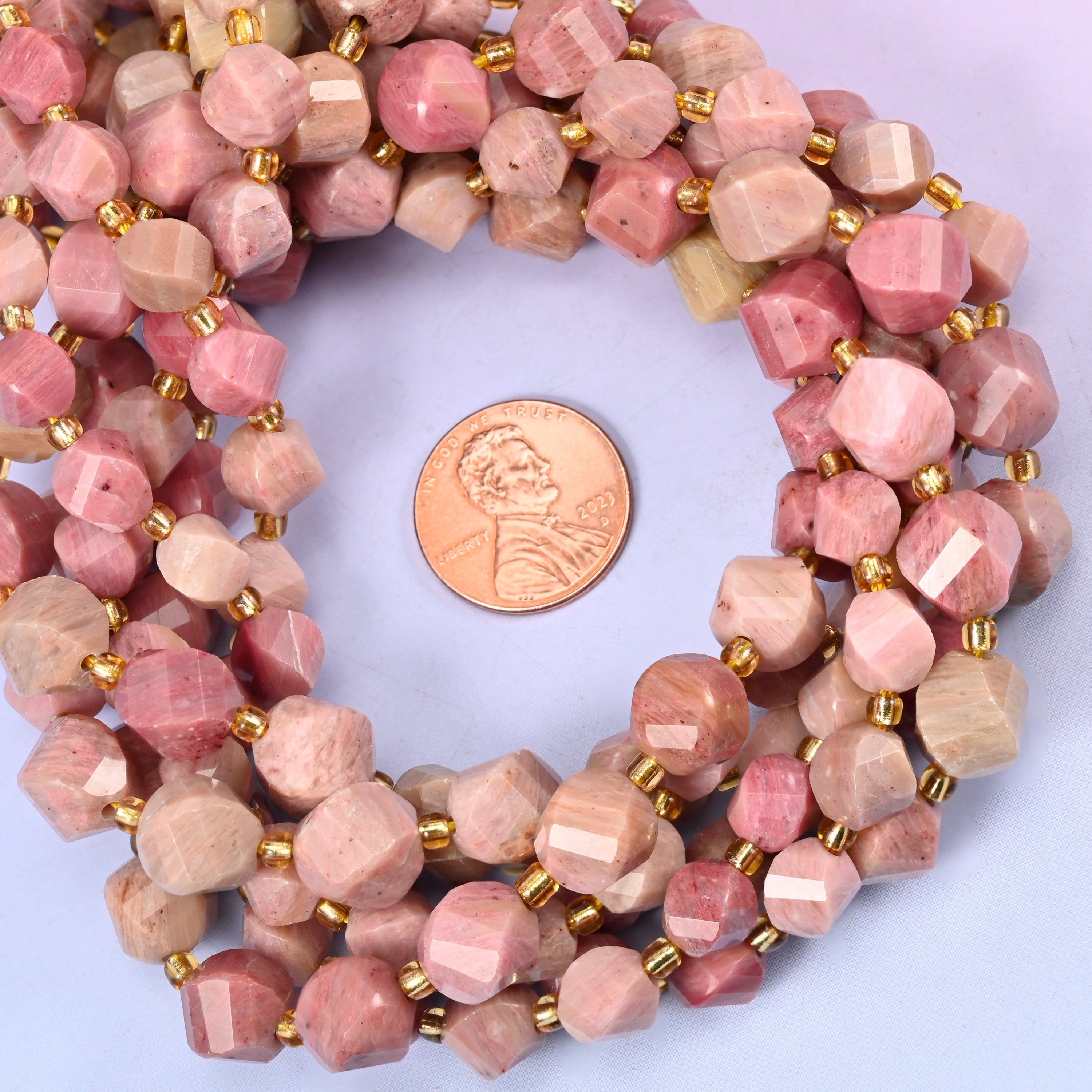 Pink Rhodonite faceted spiral twist bead strands coiled around a US penny for size reference
