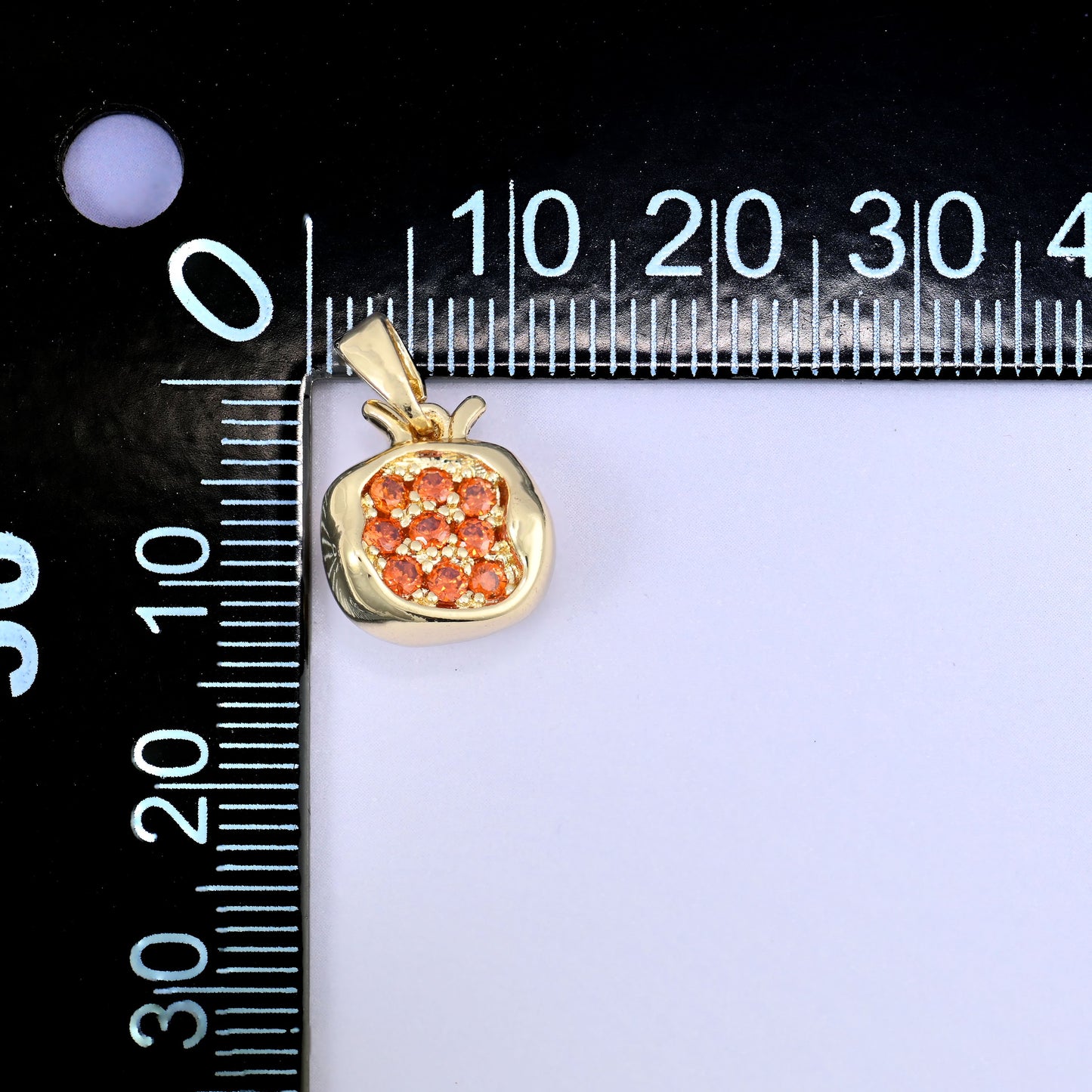 A pomegranate zircon charm photographed beside a millimetre ruler for scale