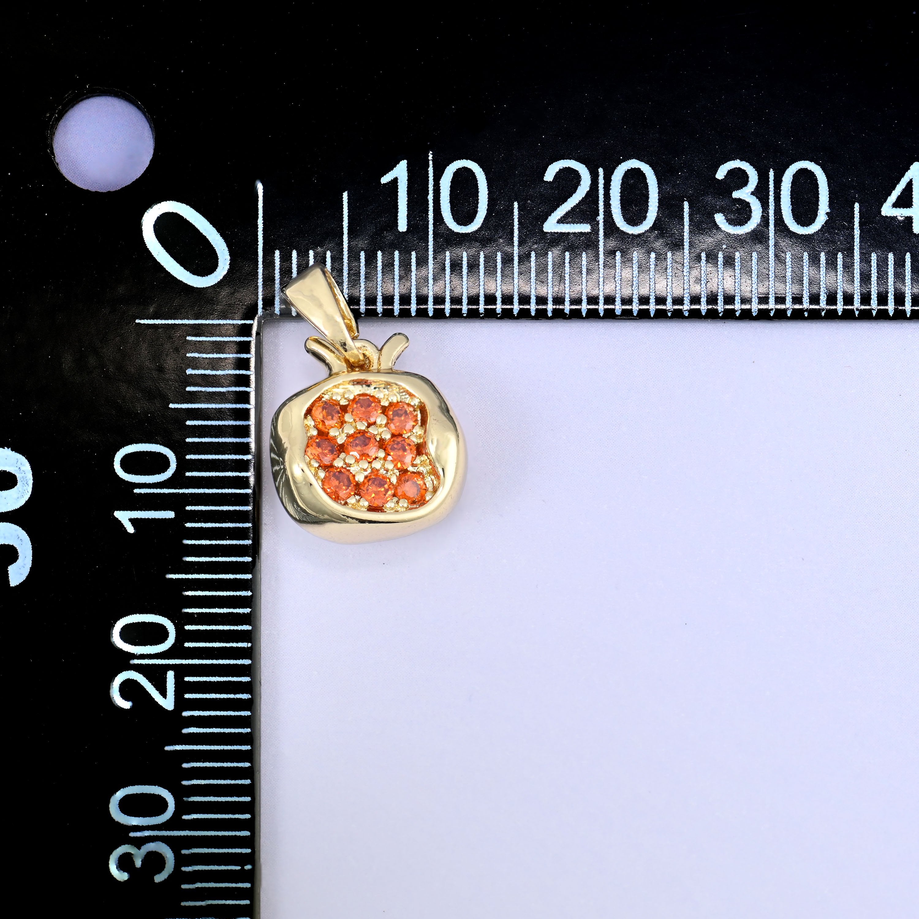 A pomegranate zircon charm photographed beside a millimetre ruler for scale