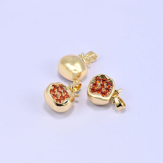 Three gold-plated pomegranate charms with orange zircon pave on a lilac background