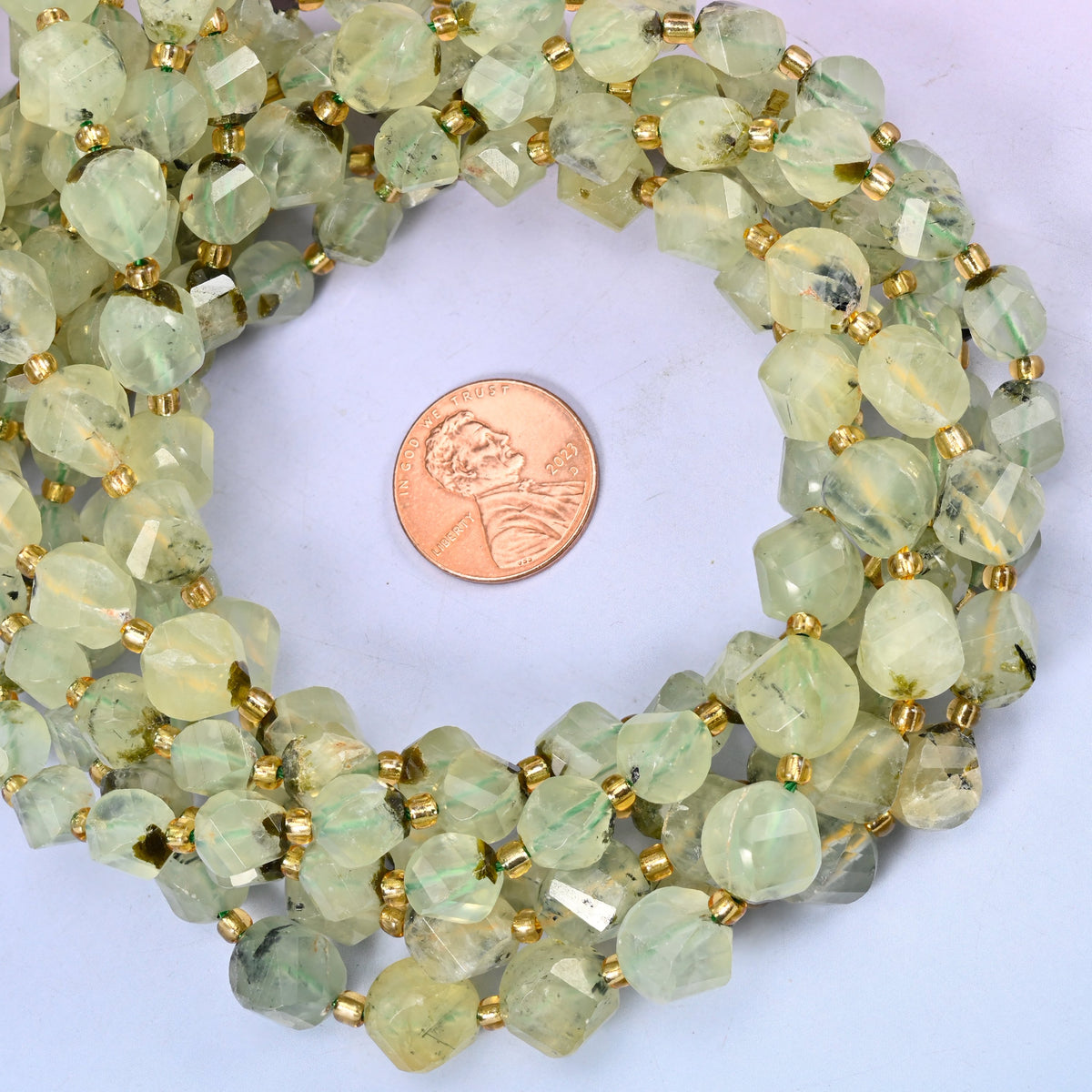 Prehnite faceted spiral twist bead strands coiled around a US penny for size reference