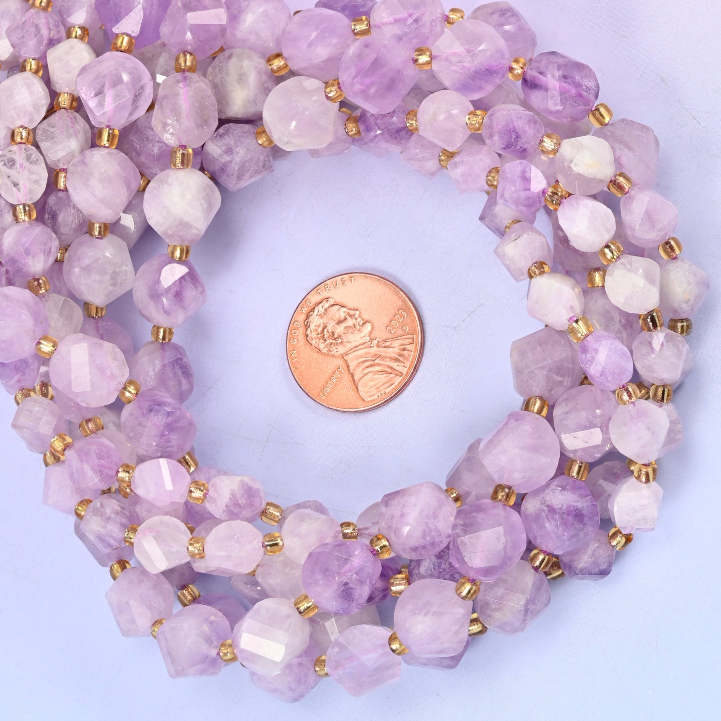 Purple Jade faceted spiral twist bead strands coiled around a US penny for size reference