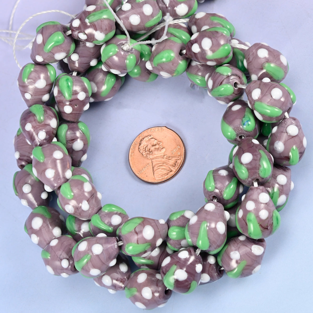Purple White Dots Strawberry glass bead strands coiled around a US penny for size reference