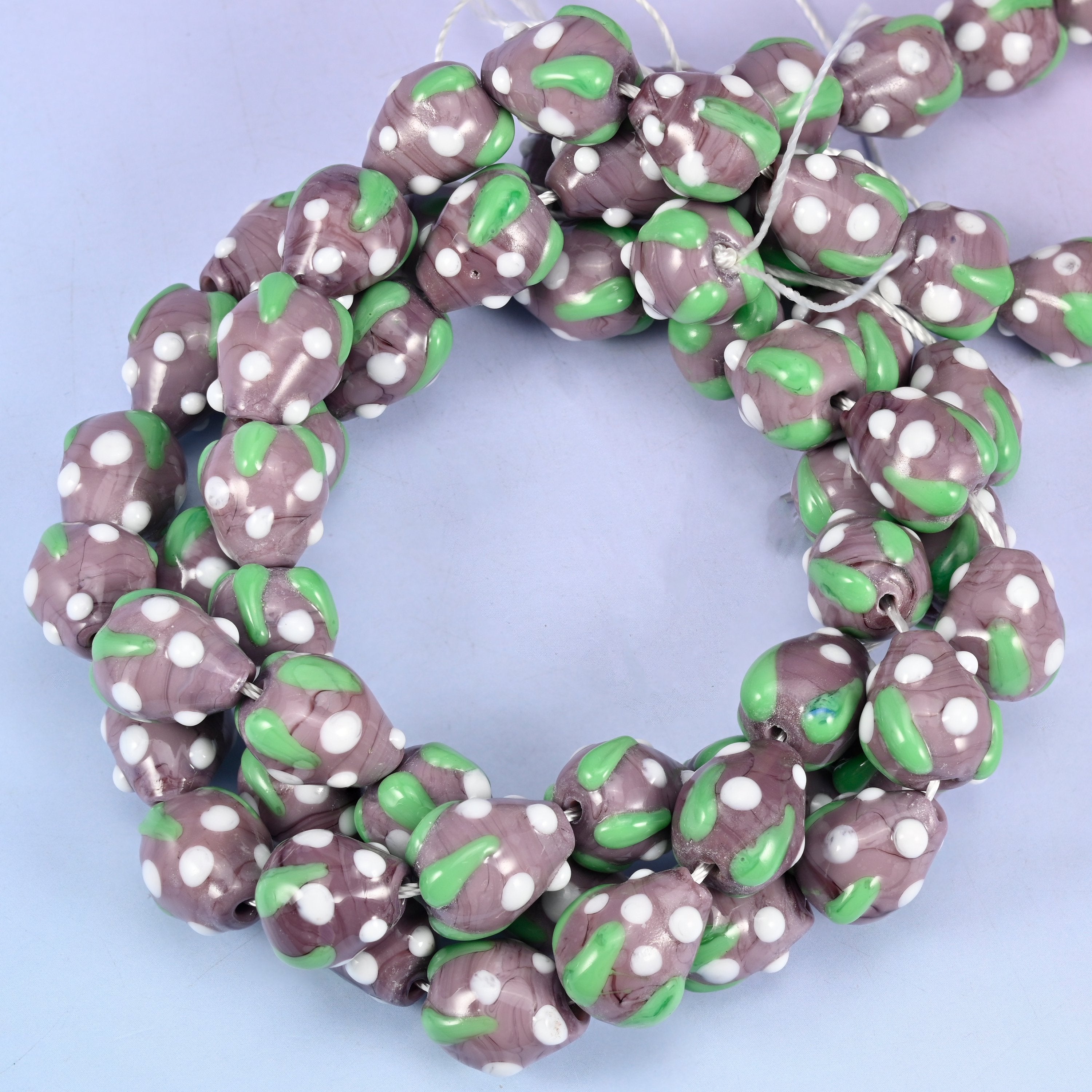 Purple White Dots Strawberry glass beads, close view of the coiled strands in dusty purple with green leaf panels and white seed dots