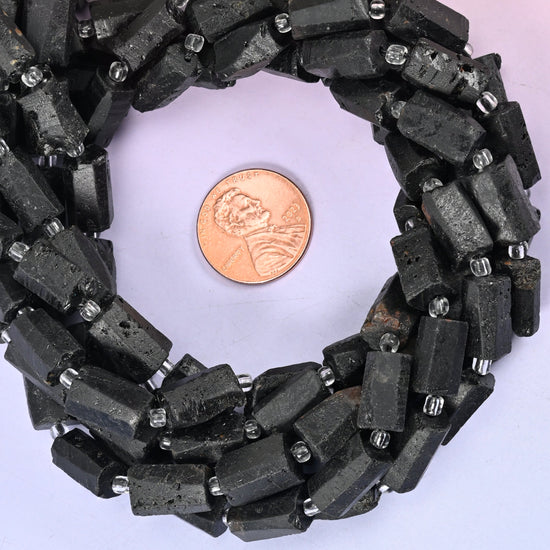 Raw Black Tourmaline faceted tube bead strands coiled around a US penny for size reference