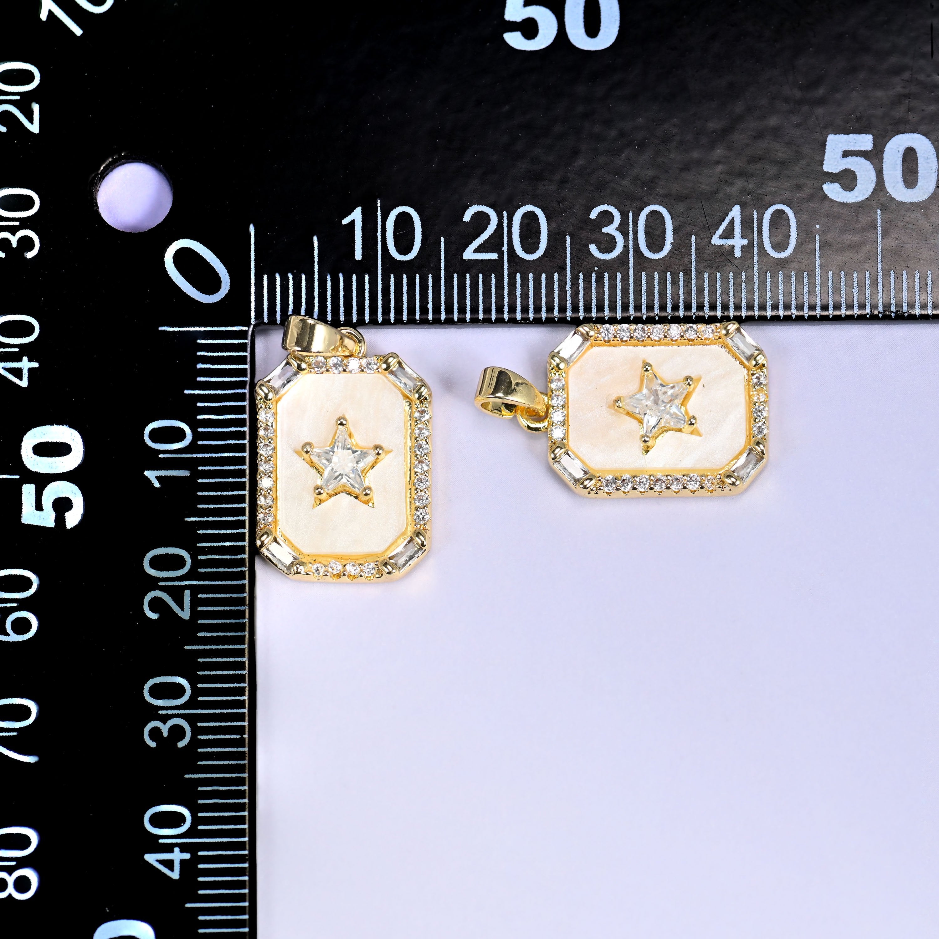 Two rectangle star charms with cream enamel and clear pave stones in a gold frame, shown front and angled, beside a millimetre ruler for scale