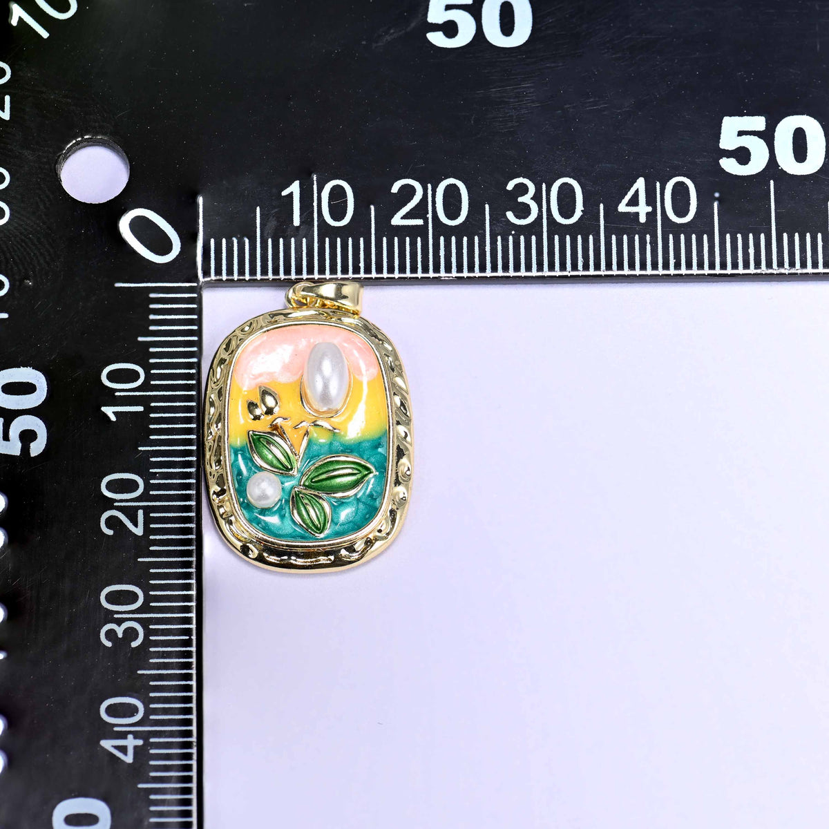 A rectangular tulip enamel pendant photographed beside a millimetre ruler for scale