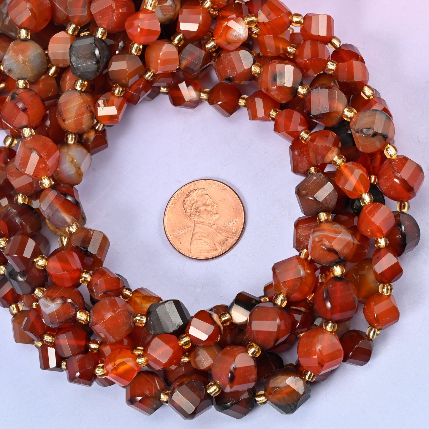 Red Agate faceted spiral twist bead strands coiled around a US penny for size reference