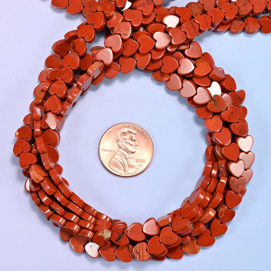 Red Jasper flat heart bead strands coiled around a US penny for size reference