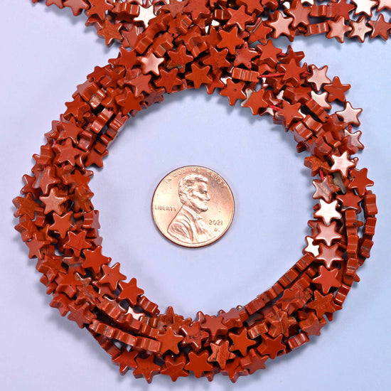 Red Jasper flat star bead strands coiled around a US penny for size reference