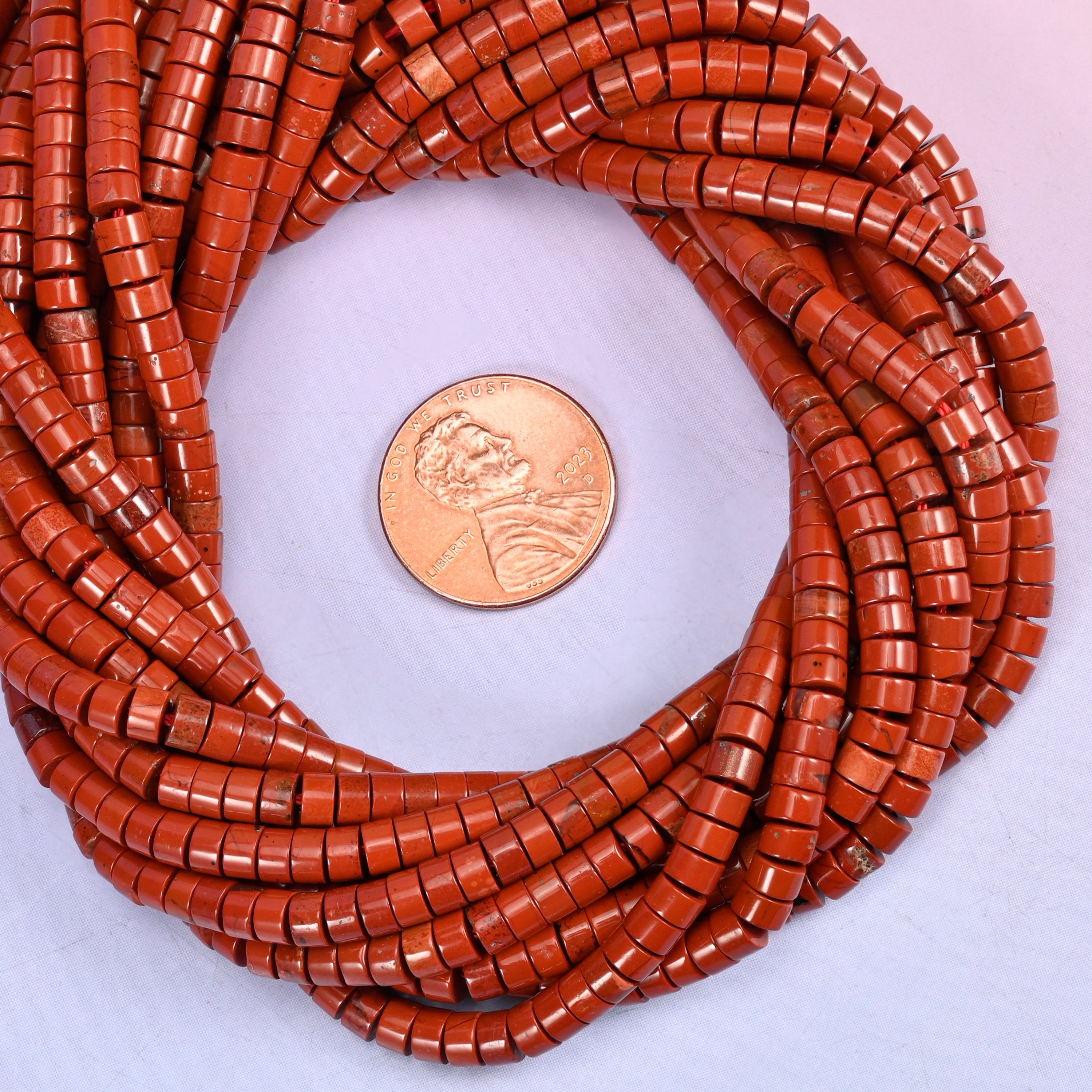 Red Jasper smooth heishi disc bead strands coiled around a US penny for size reference