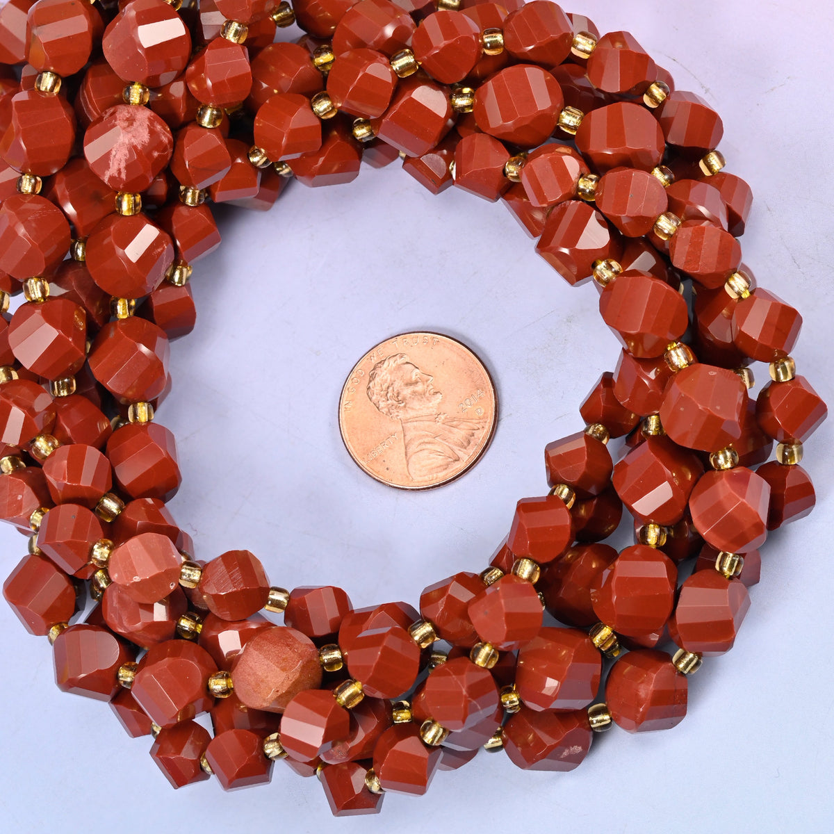 Red Jasper faceted spiral twist bead strands coiled around a US penny for size reference
