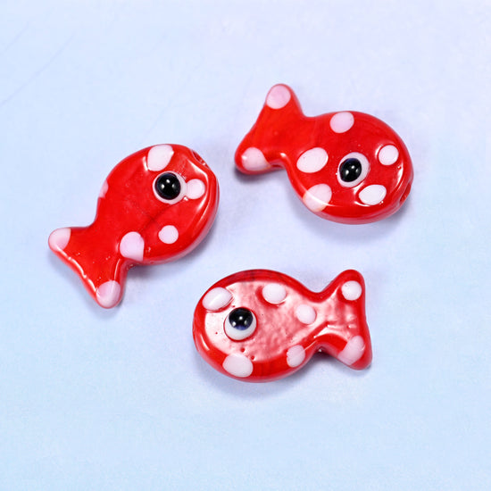 Three red fish glass beads with white dots and black eyes, close detail on a plain background
