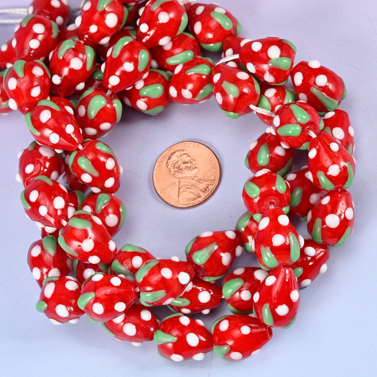 Red White Dots Strawberry glass bead strands coiled around a US penny for size reference