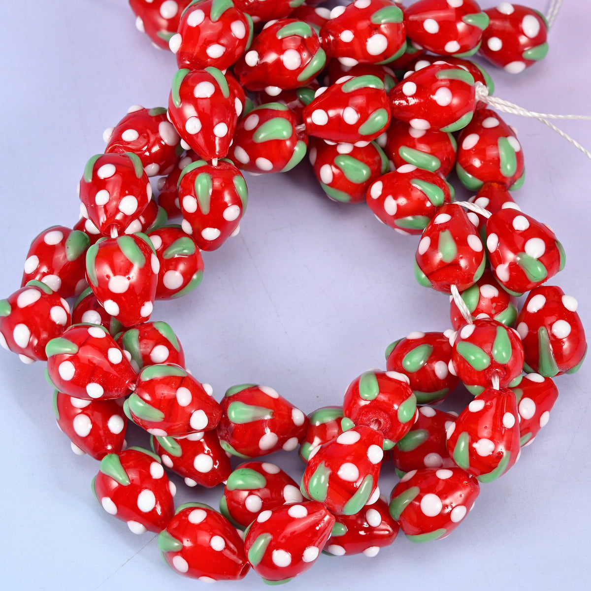 Red White Dots Strawberry glass beads, close view of the coiled strands in red with green leaf panels and white seed dots