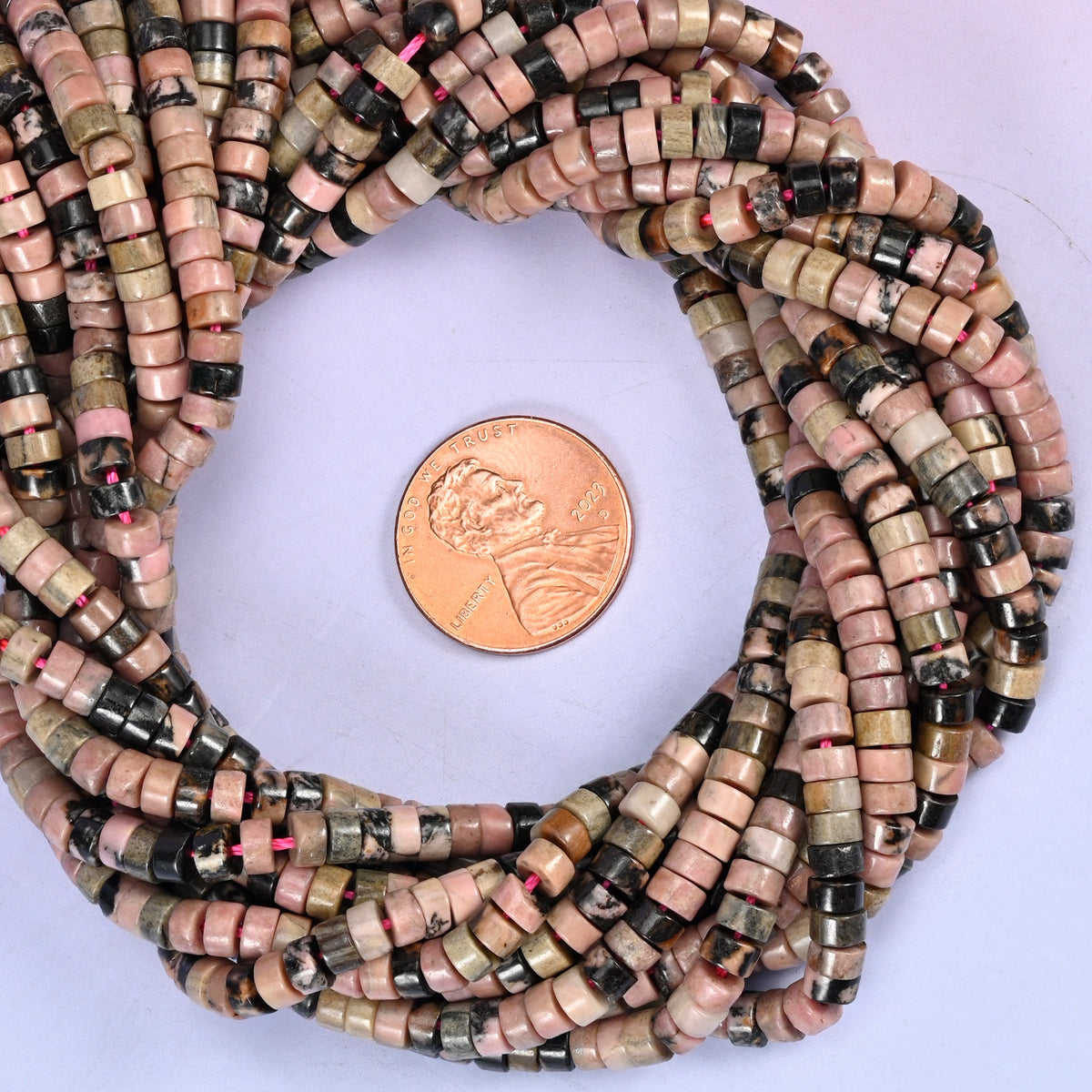 Rhodonite smooth heishi disc bead strands coiled around a US penny for size reference