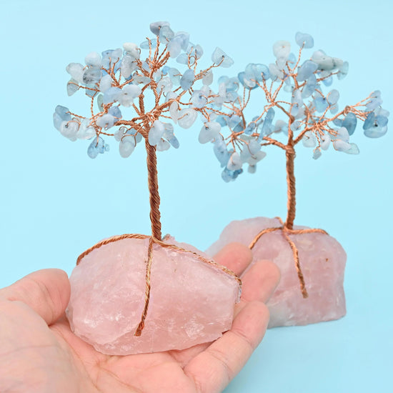 Two rose quartz base gemstone trees with copper wire branches and pale aqua chip leaves, one held in a hand for scale
