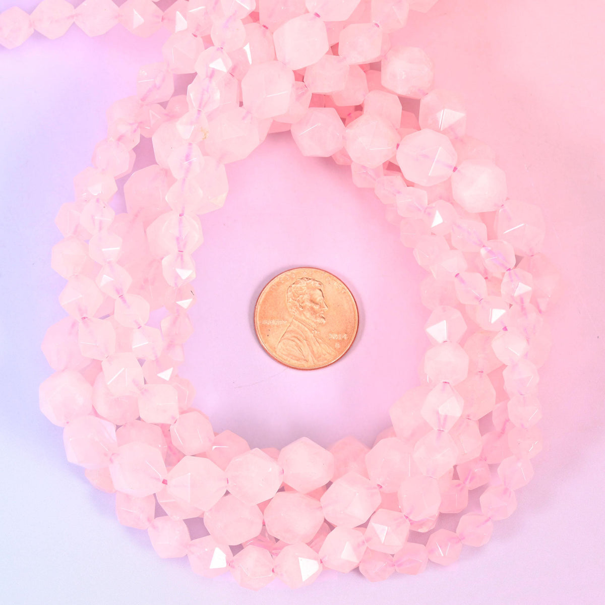 Rose quartz faceted diamond star cut bead strands coiled around a US penny for size reference