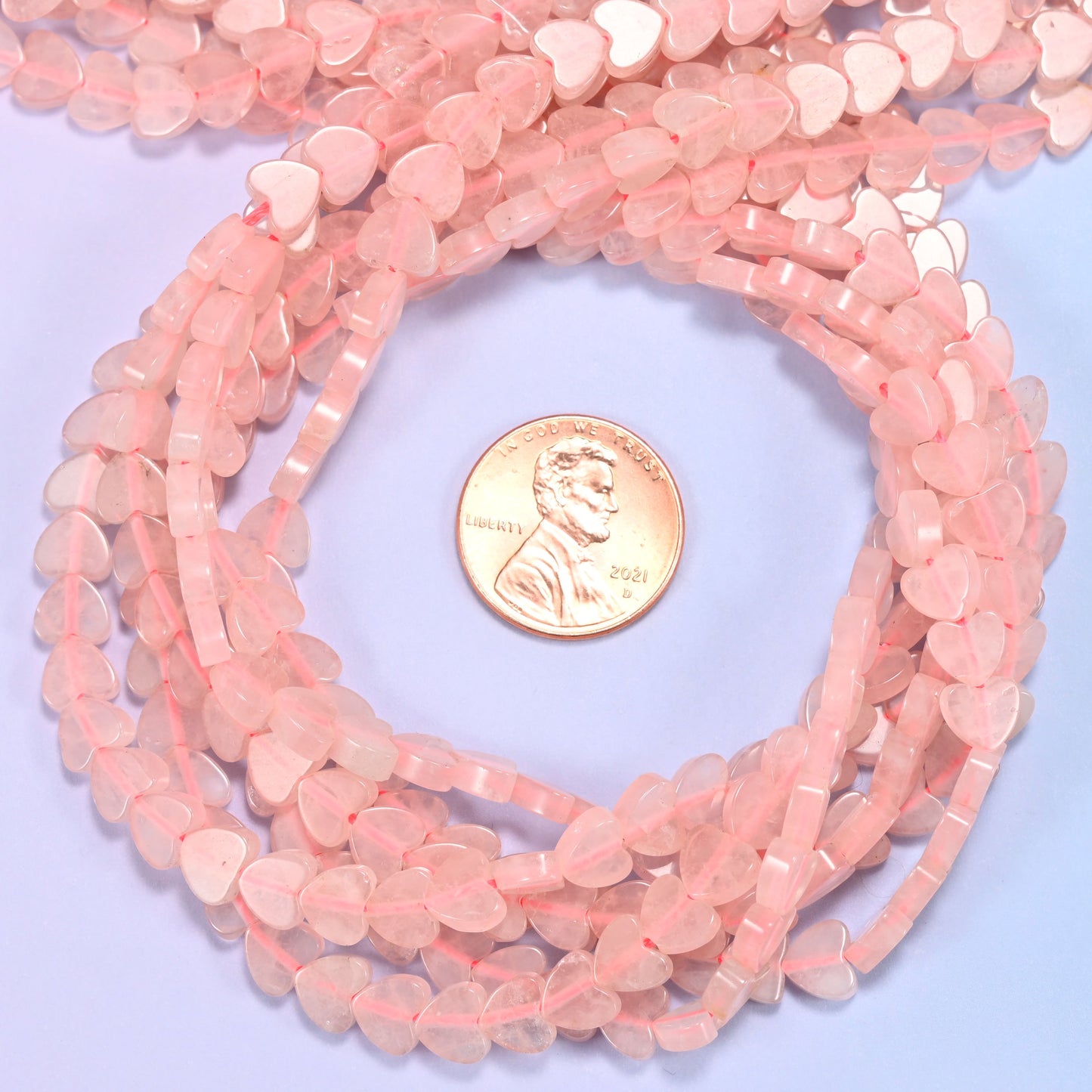Rose Quartz flat heart bead strands coiled around a US penny for size reference