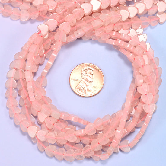 Rose Quartz flat heart bead strands coiled around a US penny for size reference