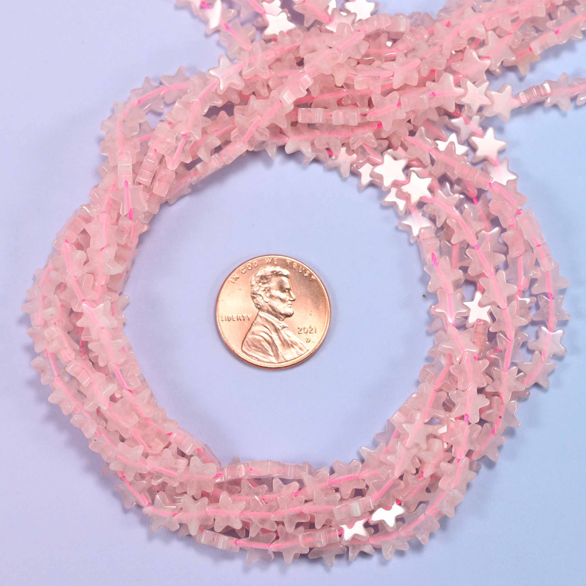 Rose Quartz flat star bead strands coiled around a US penny for size reference