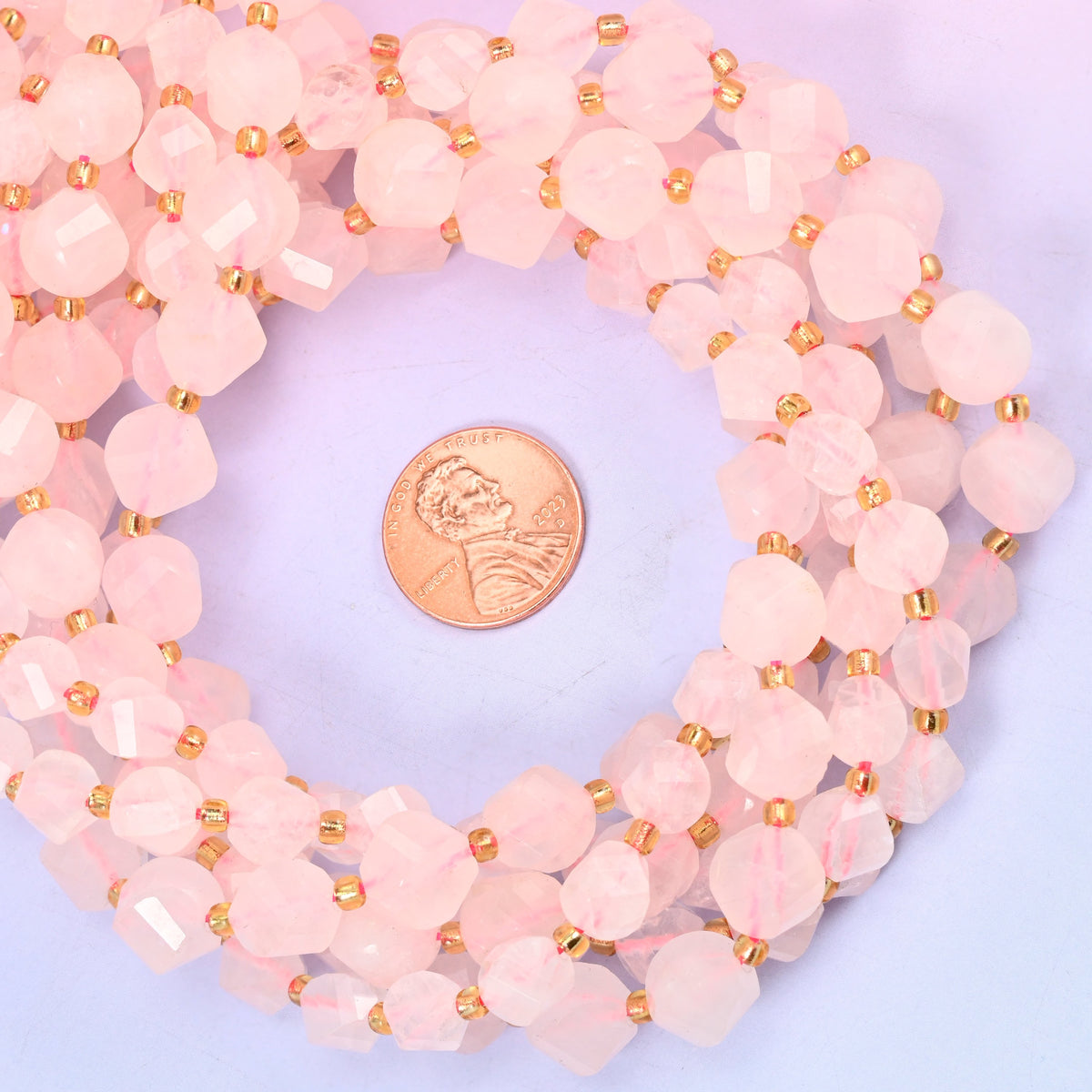 Rose Quartz faceted spiral twist bead strands coiled around a US penny for size reference