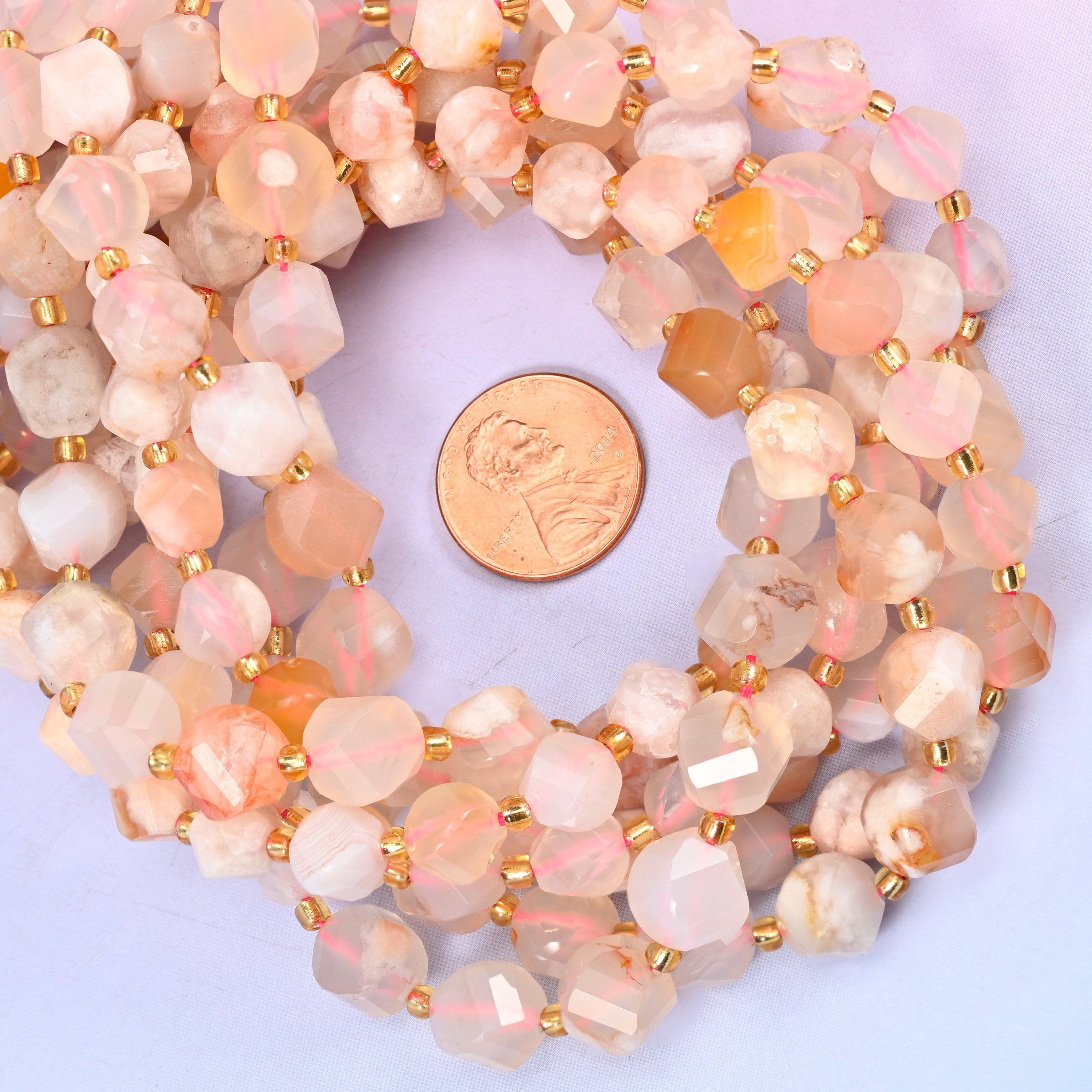 Sakura Flower Agate faceted spiral twist bead strands coiled around a US penny for size reference