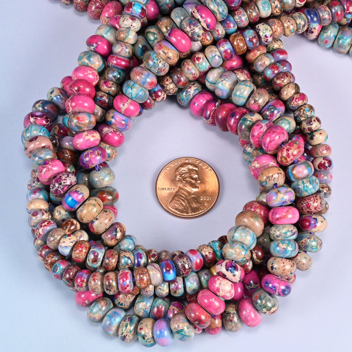 Dyed Sea Sediment Jasper rondelle bead strands coiled around a US penny for size reference