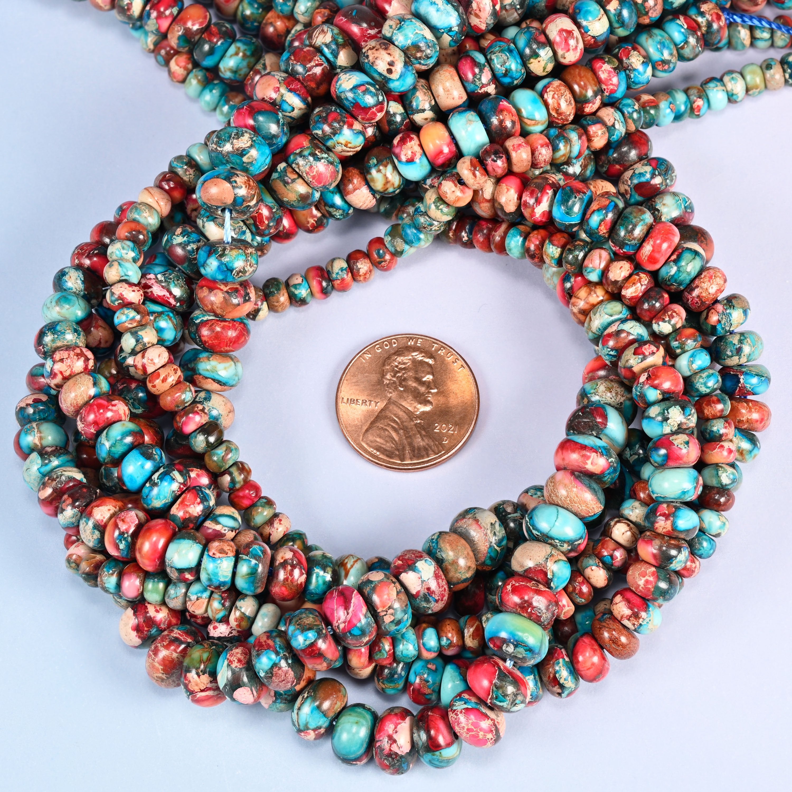 Dyed Sea Sediment Jasper rondelle bead strands coiled around a US penny for size reference