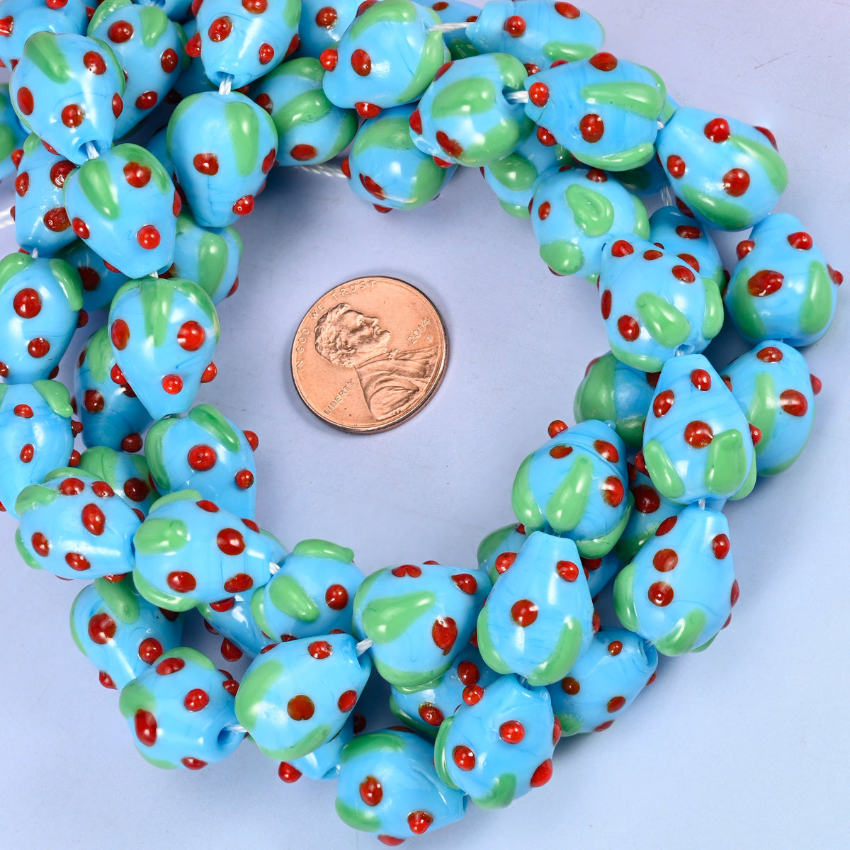 Sky Blue Red Dots Strawberry glass bead strands coiled around a US penny for size reference