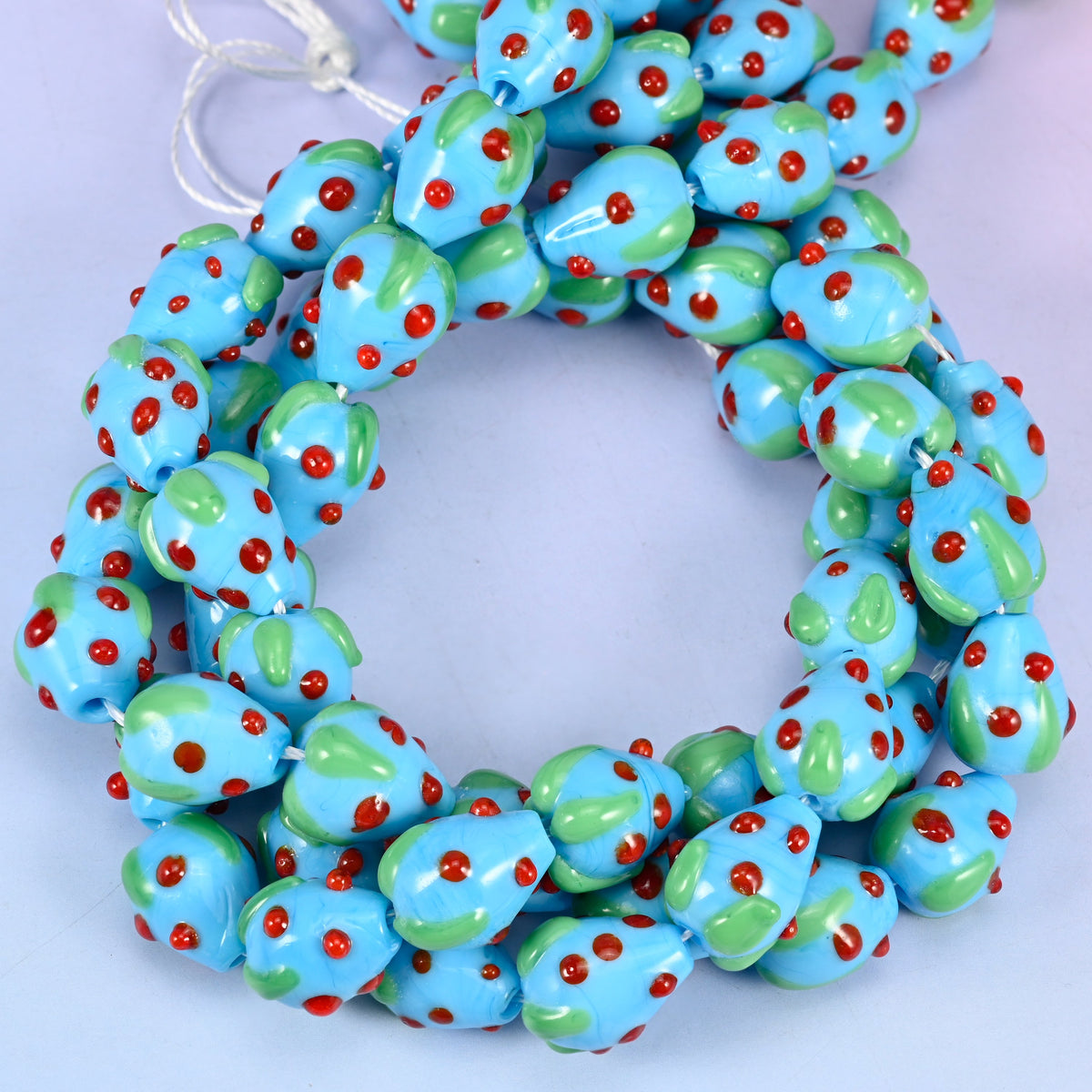 Sky Blue Red Dots Strawberry glass beads, close view of the coiled strands in sky blue with green leaves and red seed dots