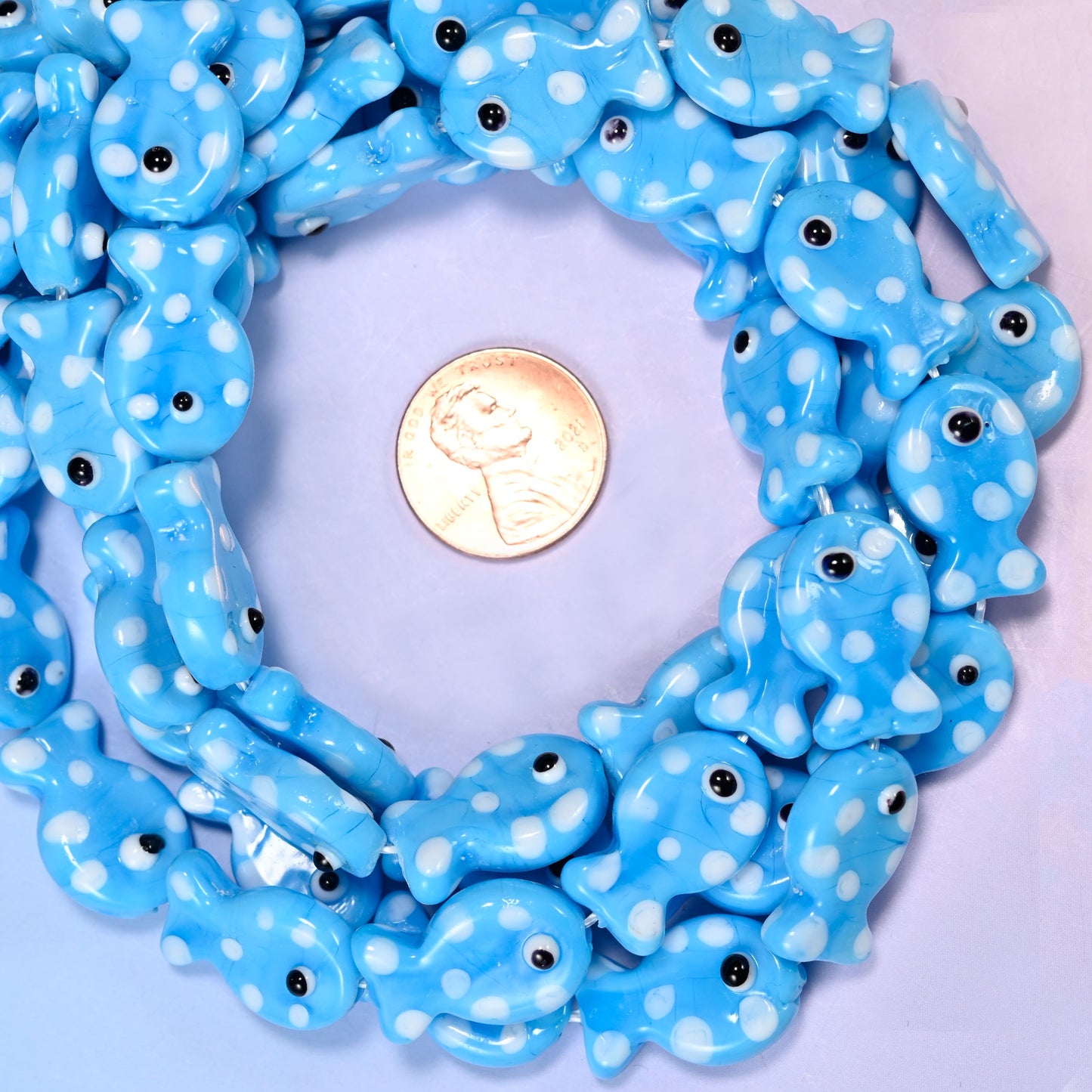Sky Blue with White Dot Fish glass bead strands coiled around a US penny for size reference