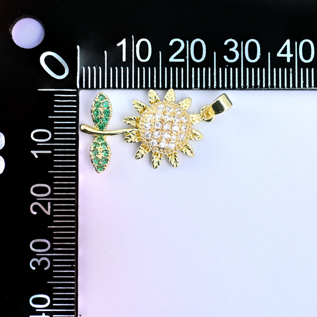 Sunflower spinner charm with a clear pave flower head, gold petals and green leaves, shown at an angle beside a millimetre ruler for scale
