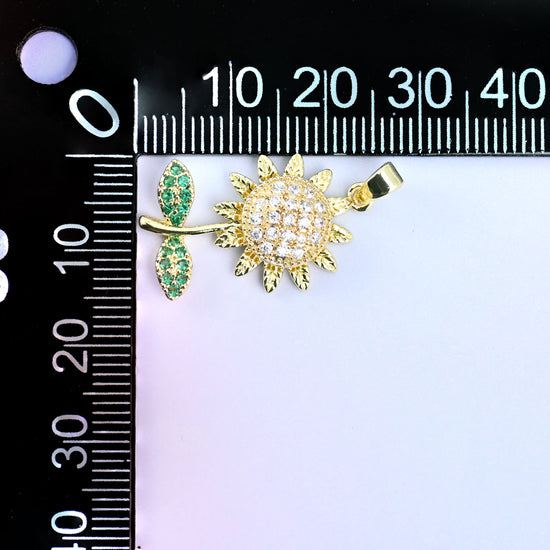 Sunflower spinner charm with a clear pave flower head, gold petals and green leaves, shown at an angle beside a millimetre ruler for scale