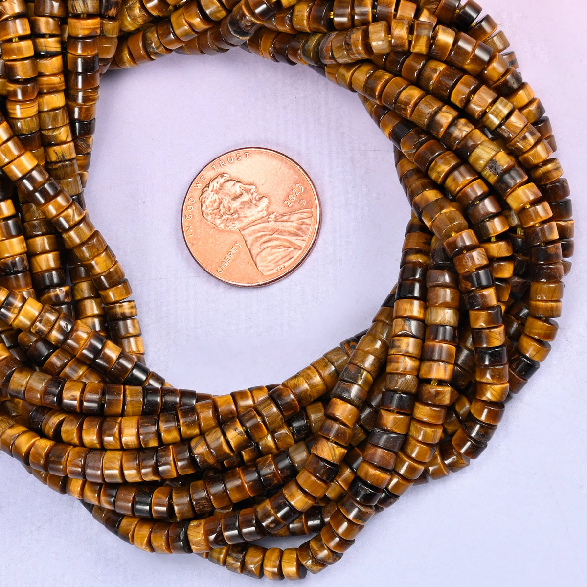Tiger Eye smooth heishi disc bead strands coiled around a US penny for size reference
