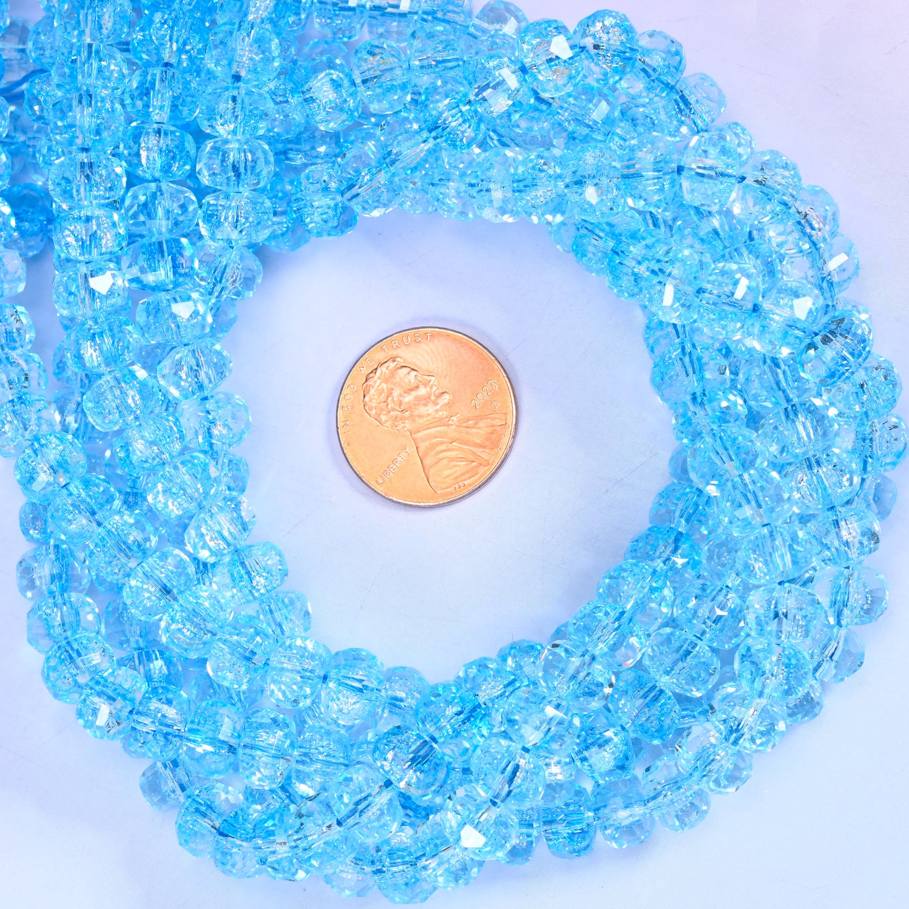 Transparent blue faceted glass rondelle strands coiled around a US penny for size reference