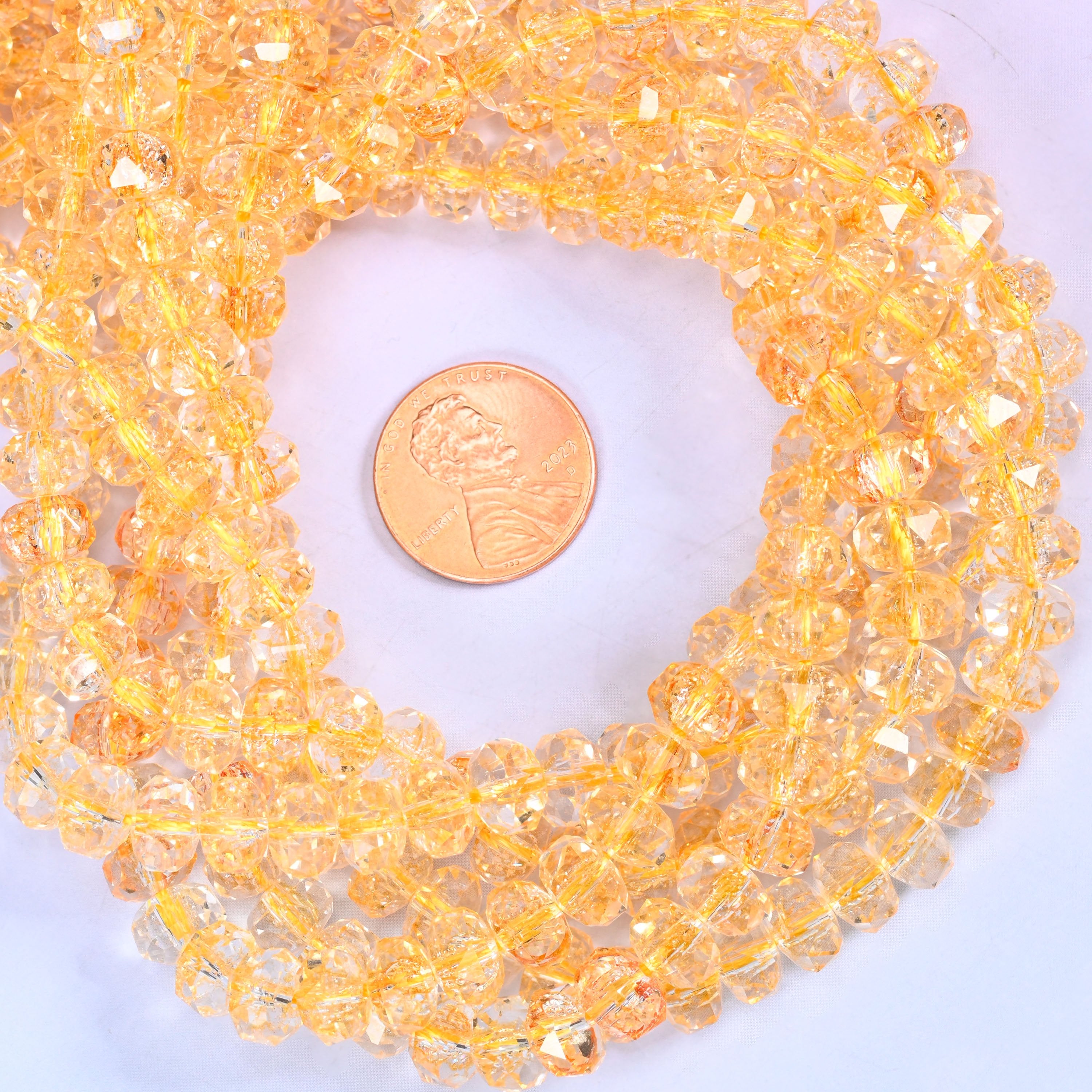 Transparent gold faceted glass rondelle strands coiled around a US penny for size reference